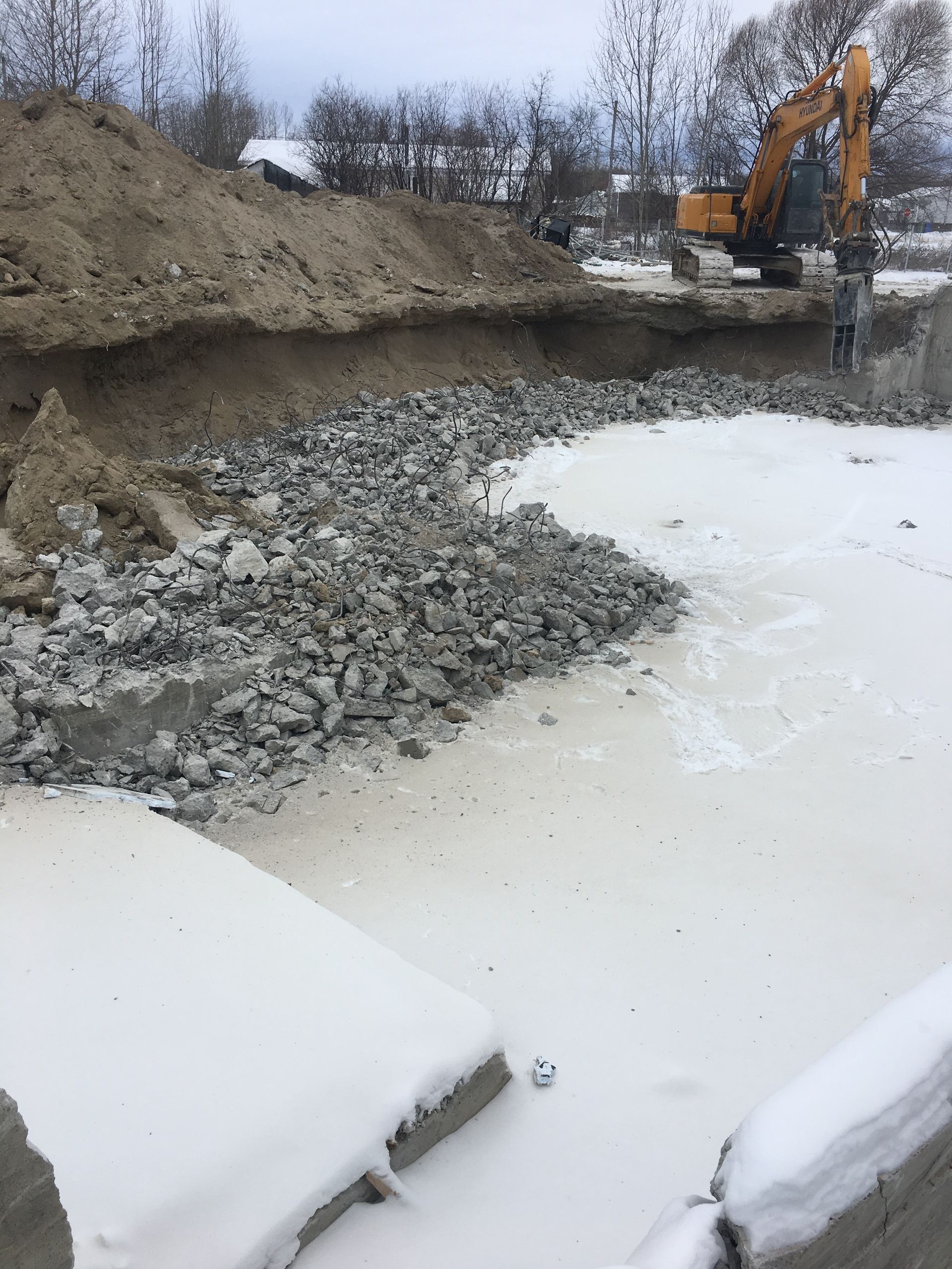 Une excavatrice creuse un trou dans la neige près d’un tas de roches.