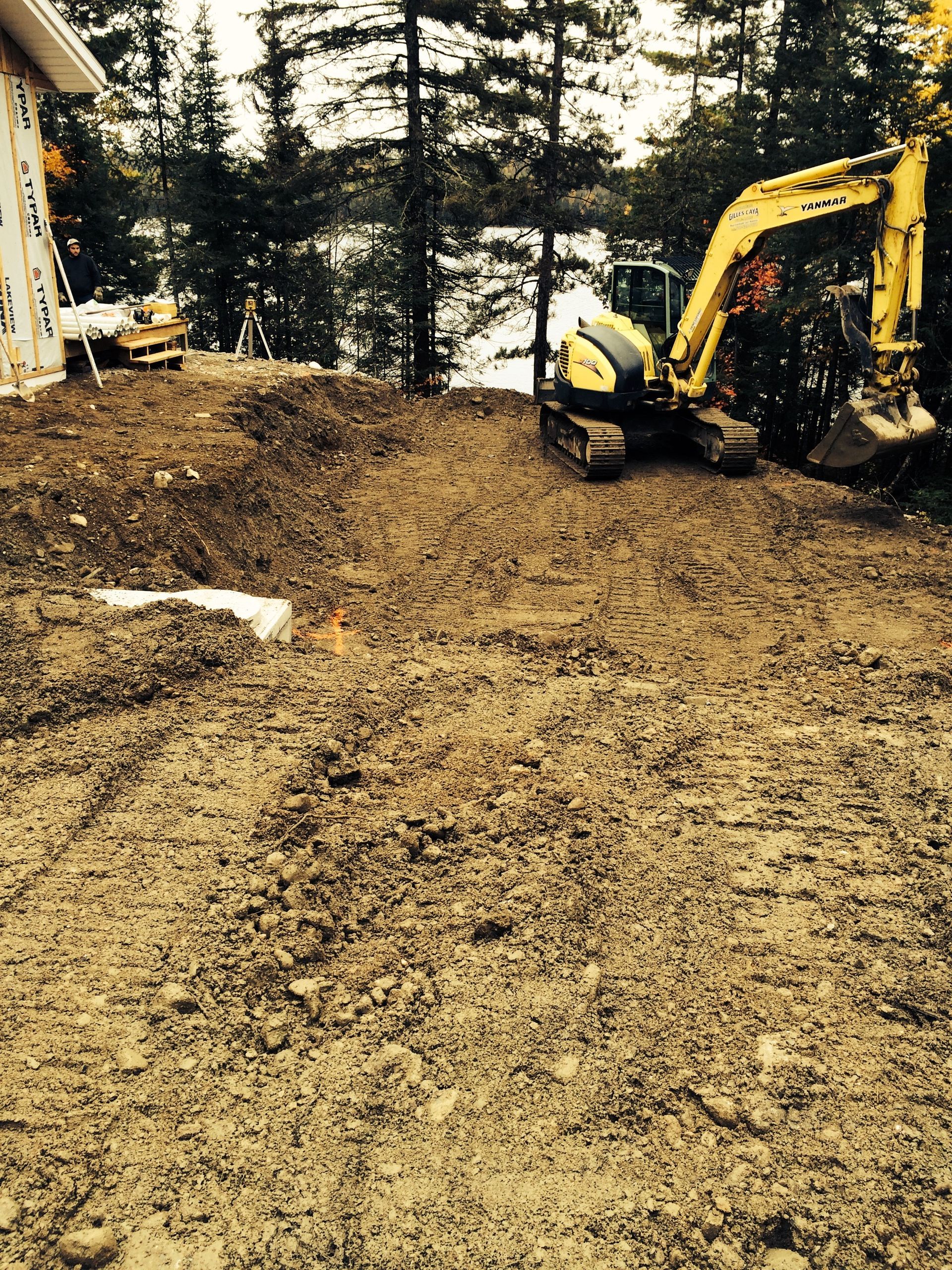 Une excavatrice jaune est assise dans la terre devant une maison.