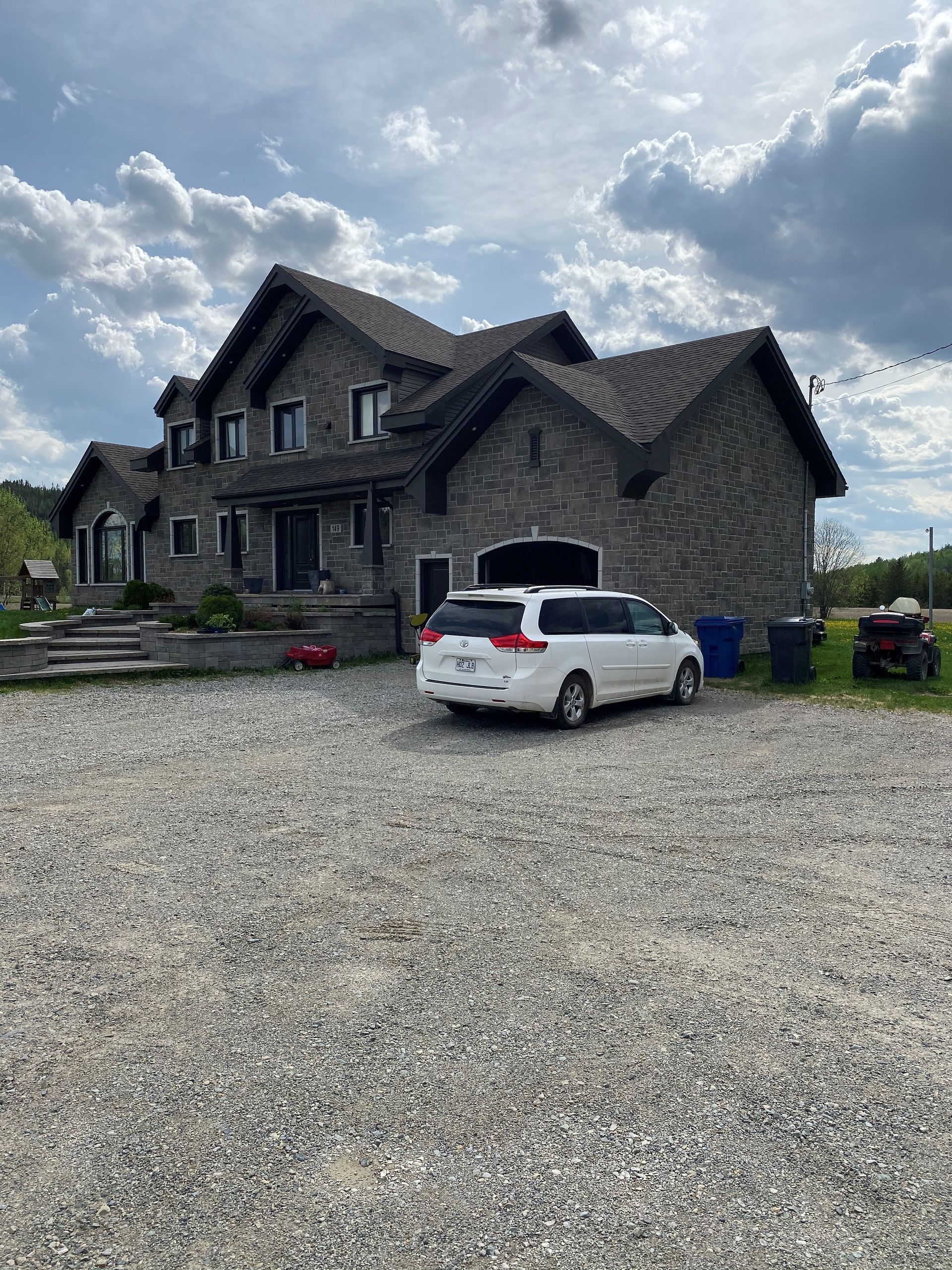 Une camionnette blanche est garée devant une grande maison en pierre.