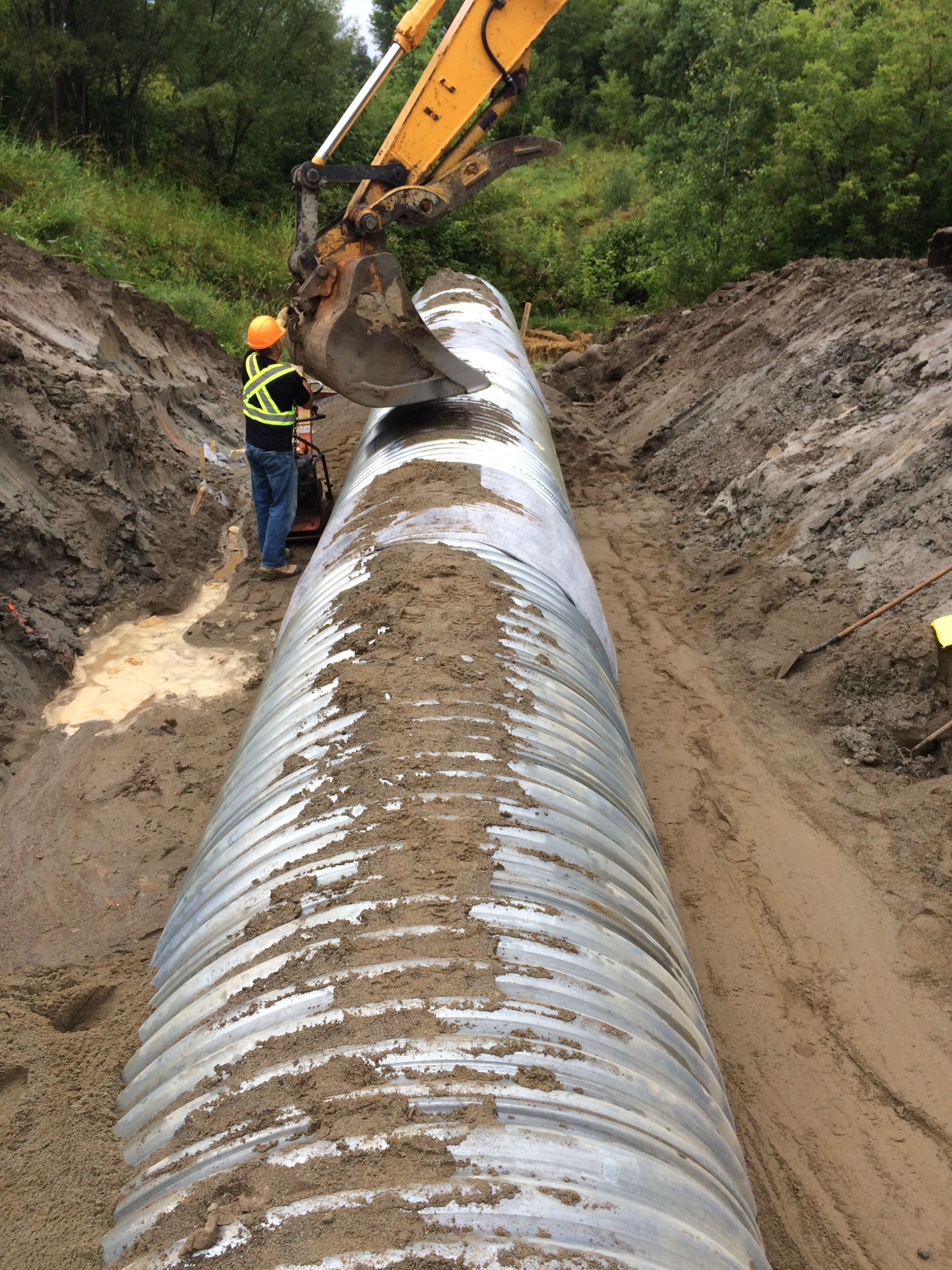 Un homme se tient à côté d’un gros tuyau dans la terre.