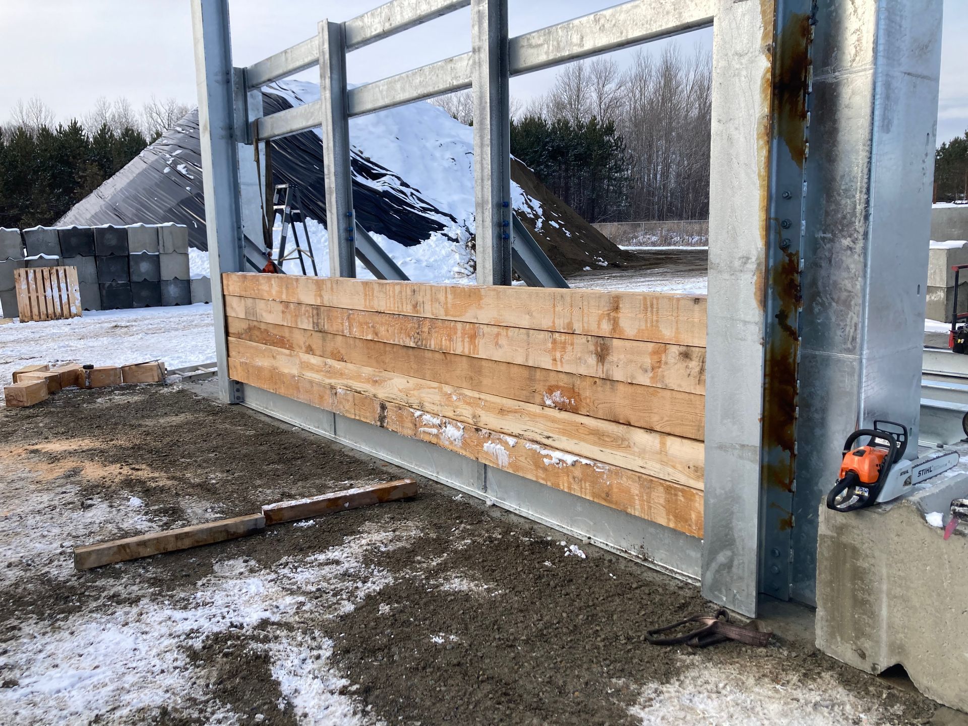 Une tronçonneuse est posée sur le sol à côté d’un mur en bois.