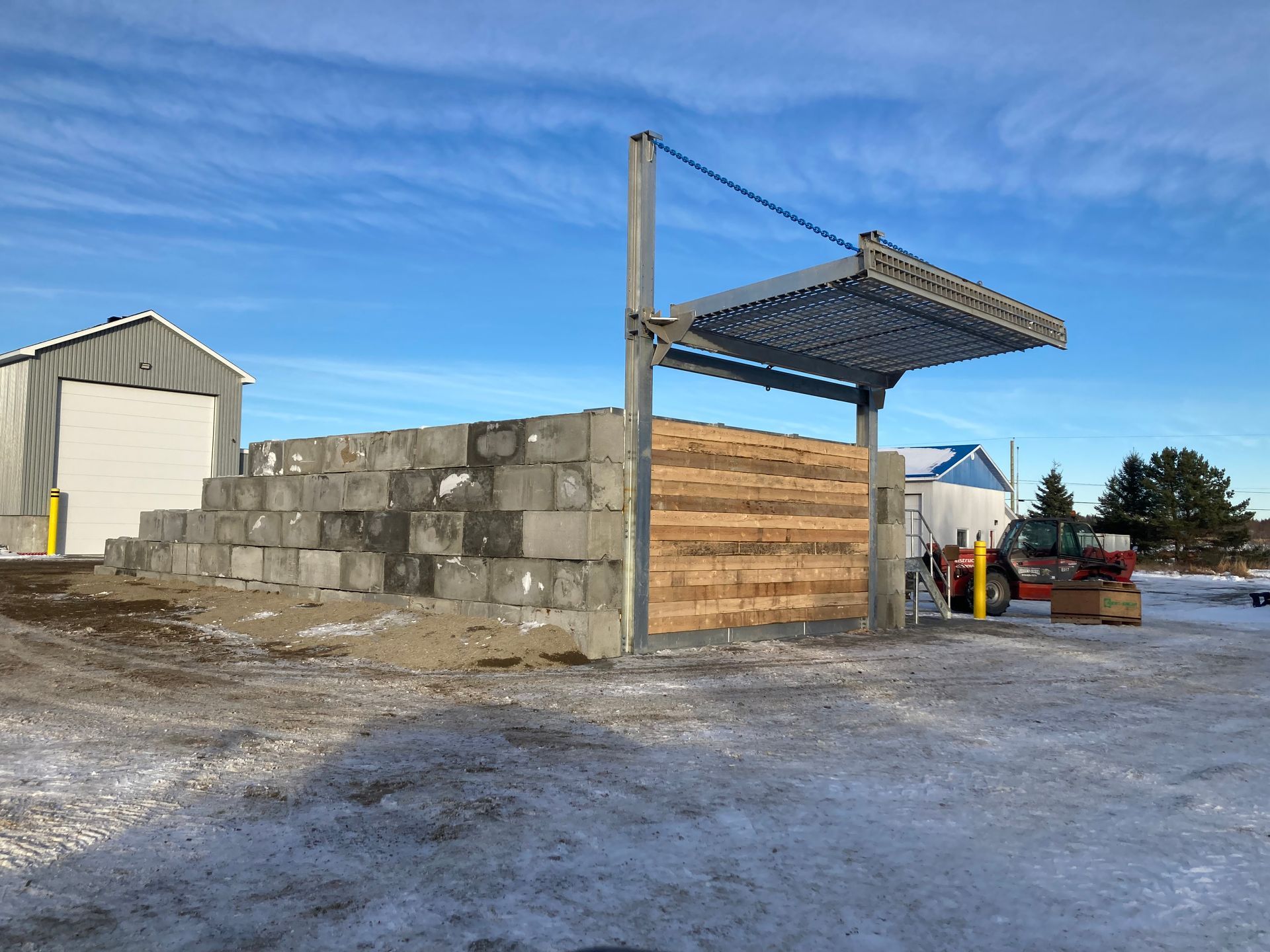 Une grande pile de blocs de béton repose dans la neige devant un garage.