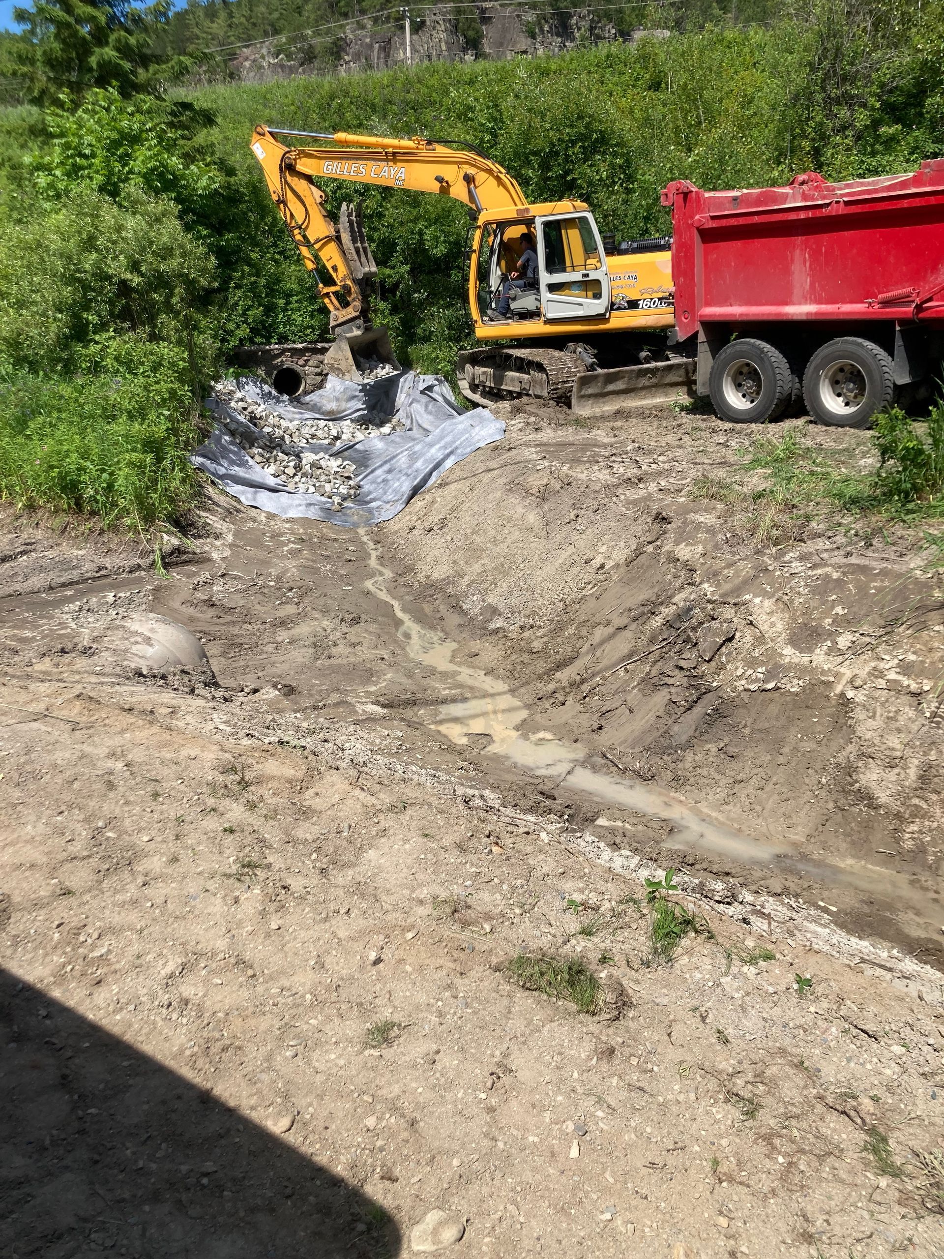 Une excavatrice jaune charge de la terre dans un camion à benne rouge.