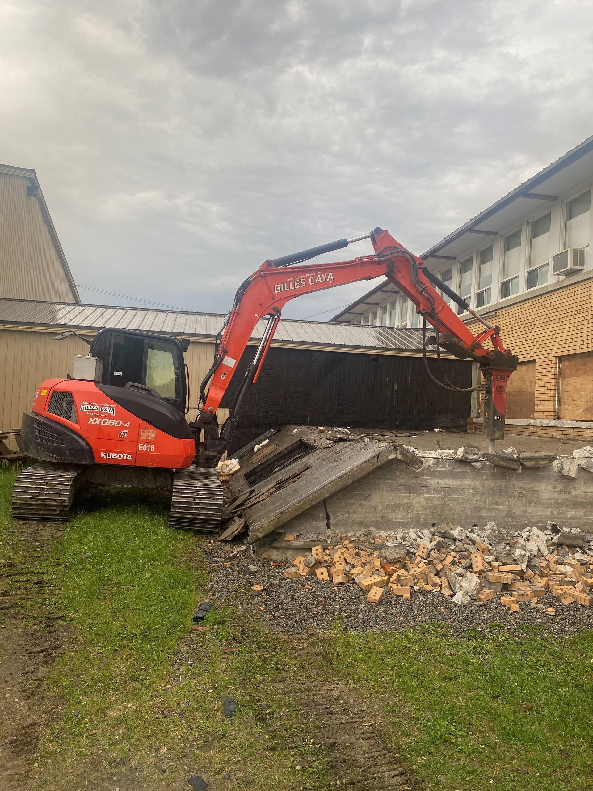 Une excavatrice rouge et noire est en train de démolir un bâtiment.