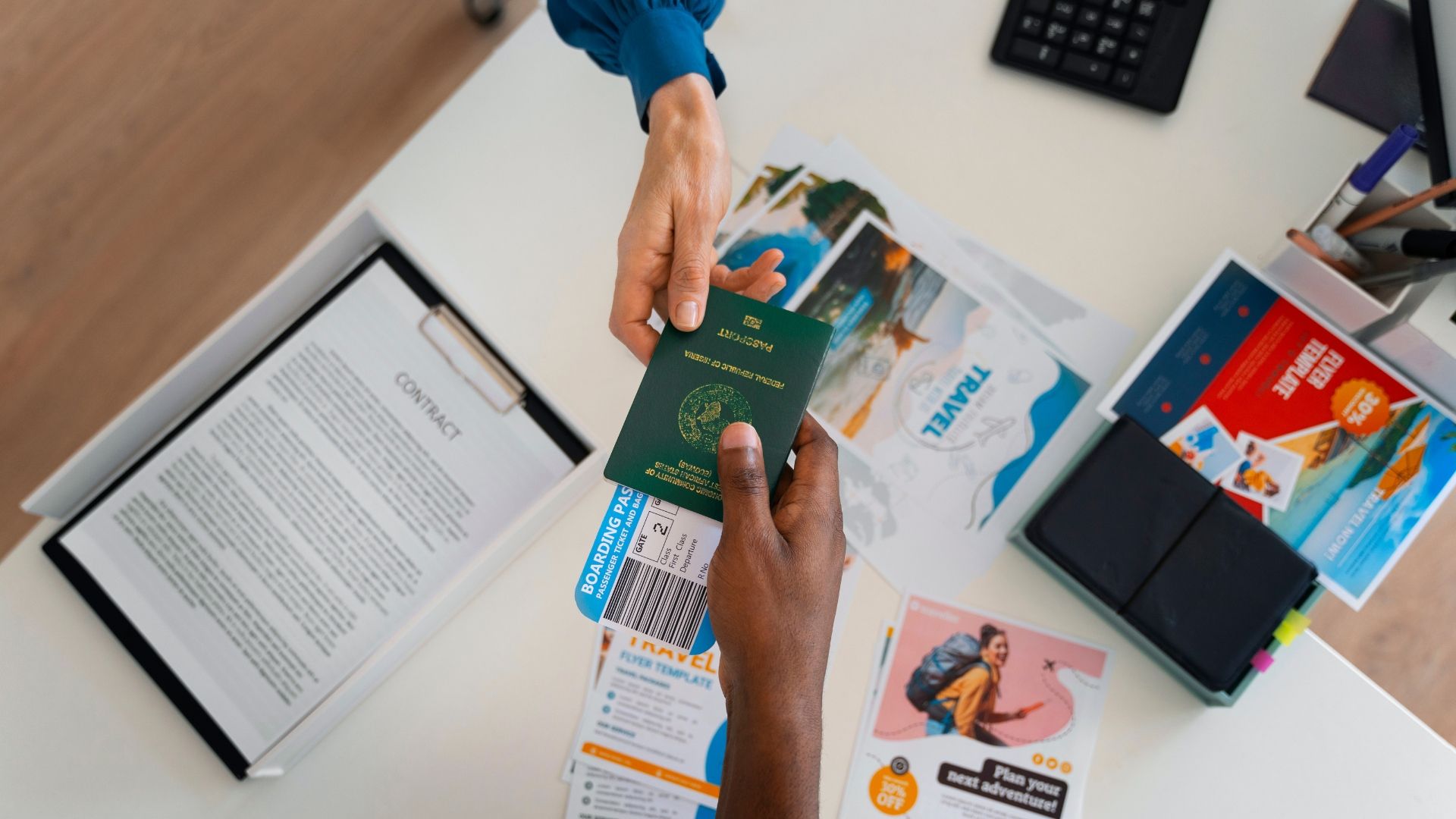 Hands exchanging a green passport over a desk with travel brochures and a contract.