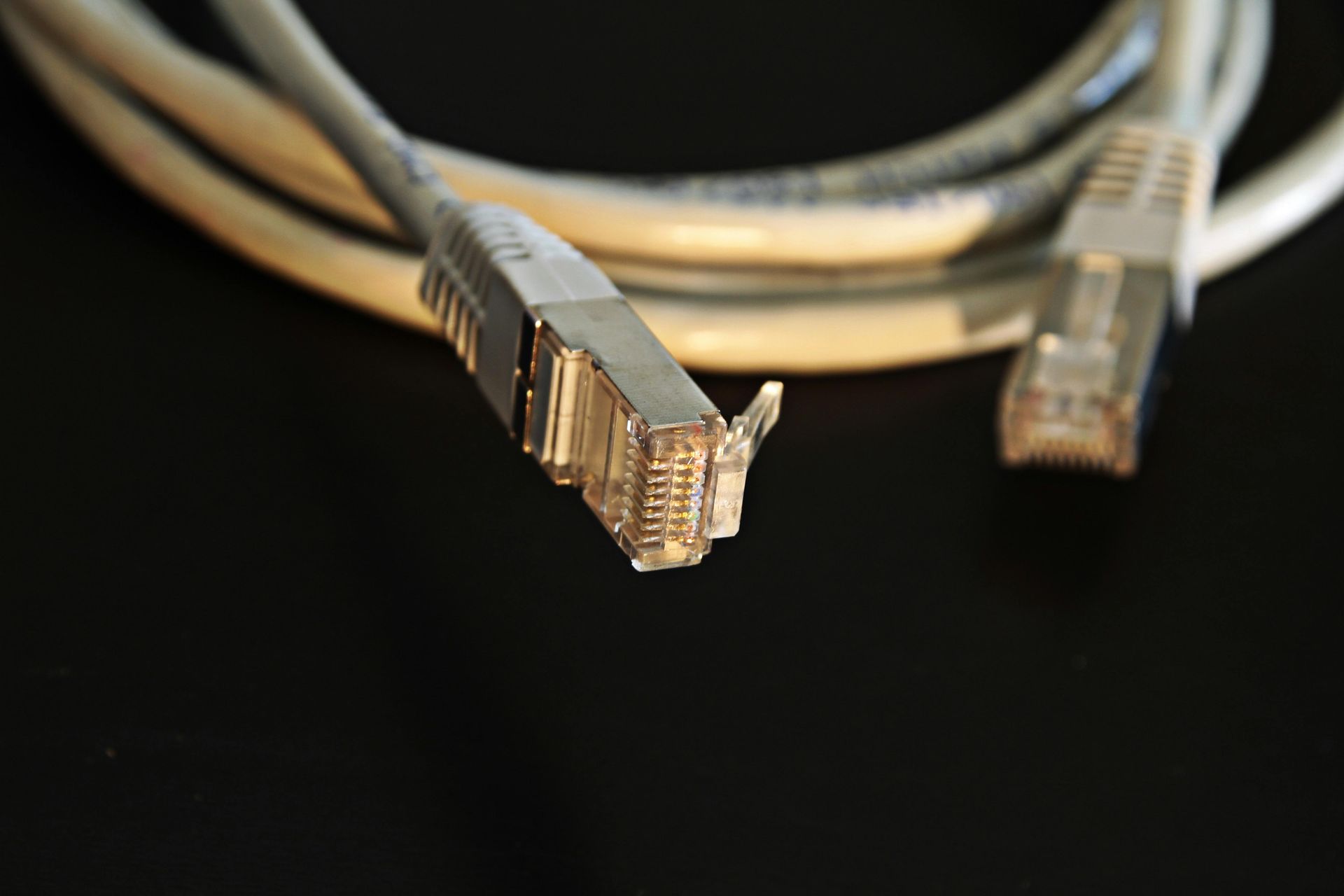 Two gray Ethernet cables with silver connectors on a black surface.