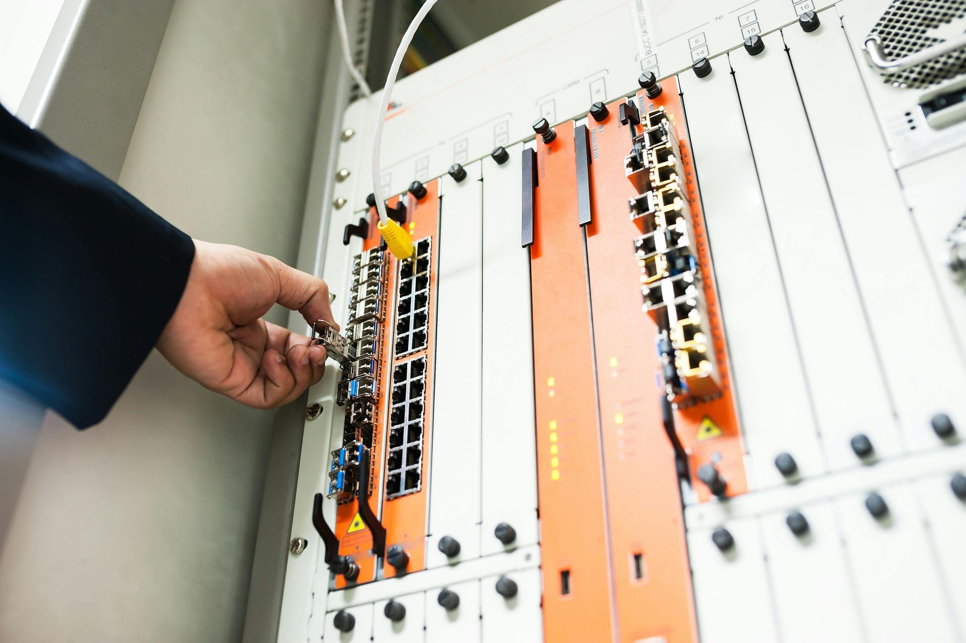 Person's hand adjusting a cable in a server rack with orange and black network cards.