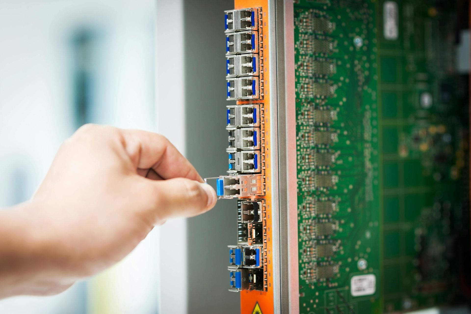 Hand inserting a blue and gray fiber optic cable into a network card on a server rack.