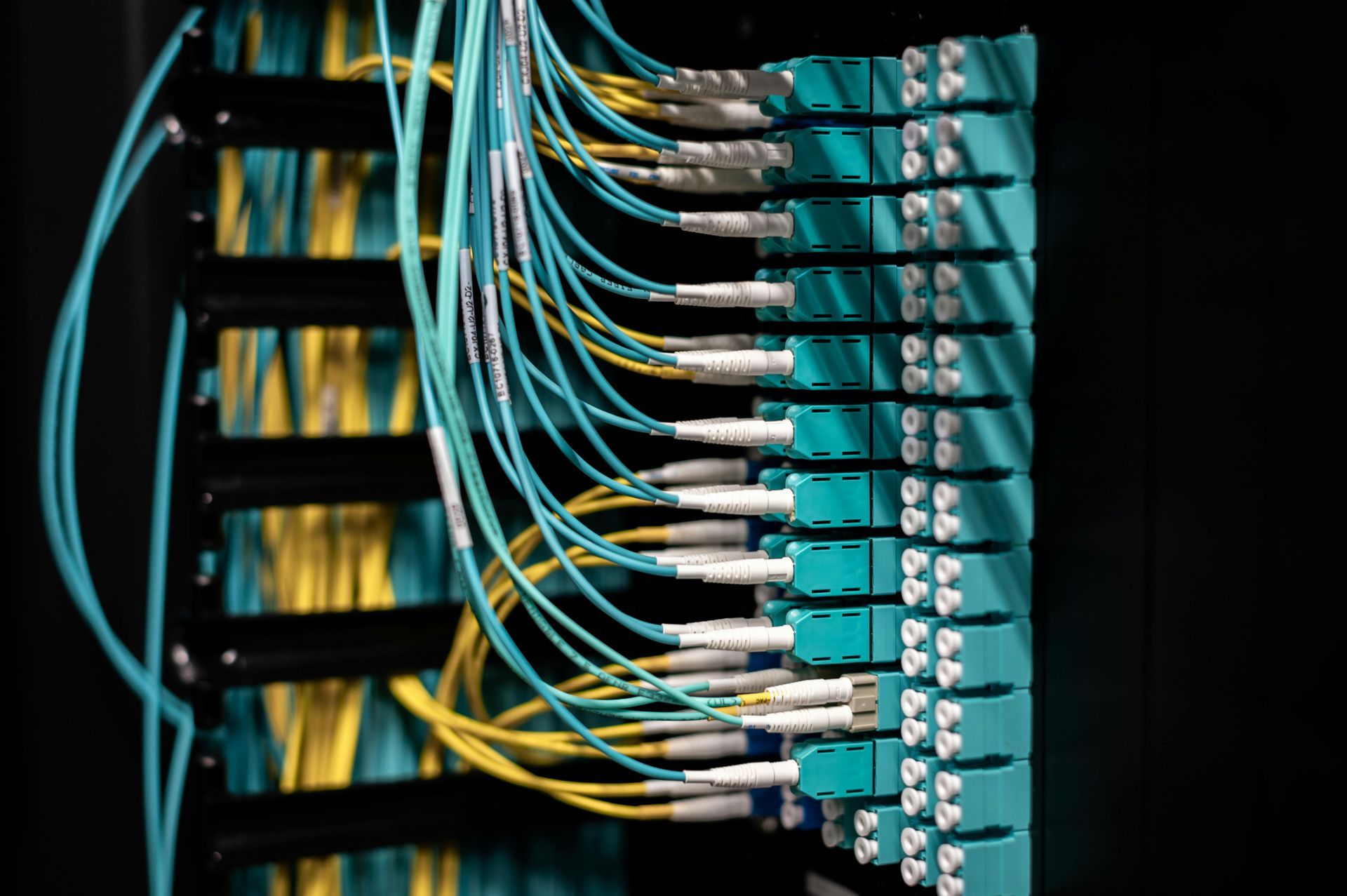 Network server rack with bundles of blue and yellow fiber optic cables connected to teal panels.