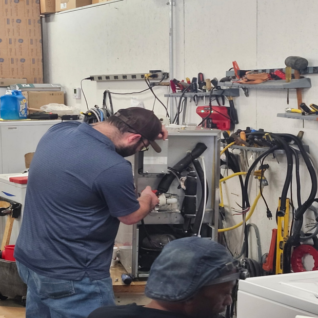 Technician working on machinery in a cluttered workshop with tools and cables on the wall