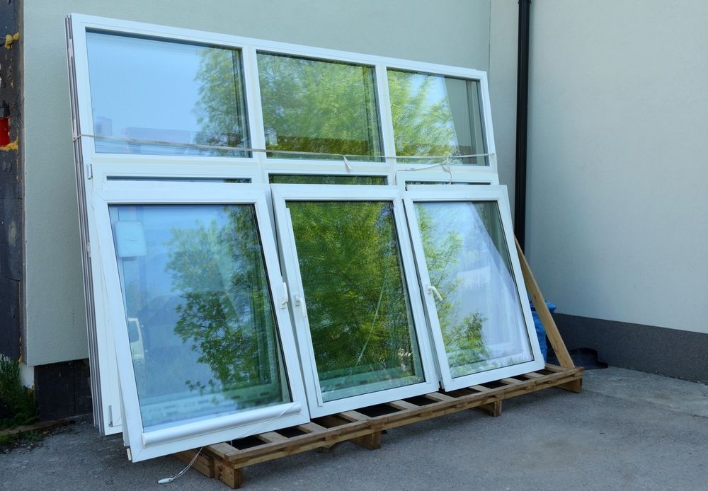 A White Framed Windows Stacked on A Wooden Pallet Outdoors — Downs Window Renewals in Harristown, QLD