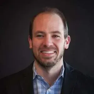 A man in a suit and plaid shirt is smiling for the camera.