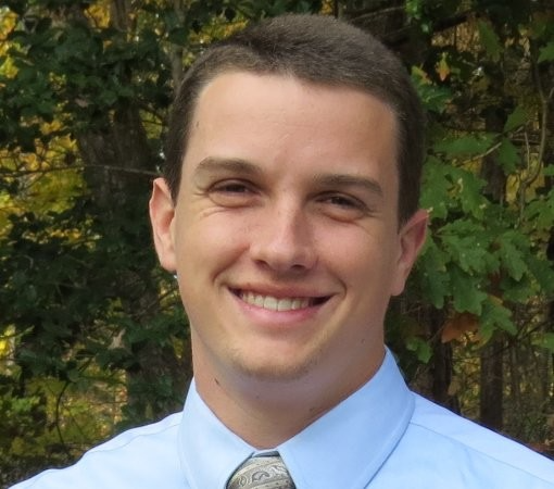 A man in a blue shirt and tie is smiling for the camera