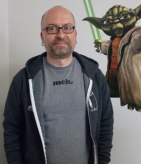 A man wearing a shirt that says meh stands in front of a picture of yoda