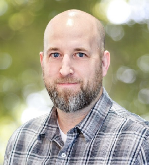 A bald man with a beard is wearing a plaid shirt.
