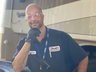 Man in work uniform, safety glasses, near RV, smiling and looking at the camera.
