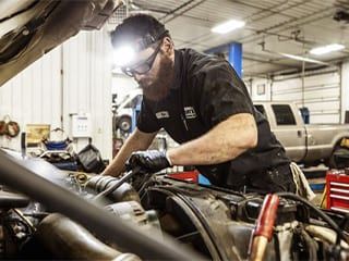 Mechanic working on an engine in a garage; wearing a headlamp.