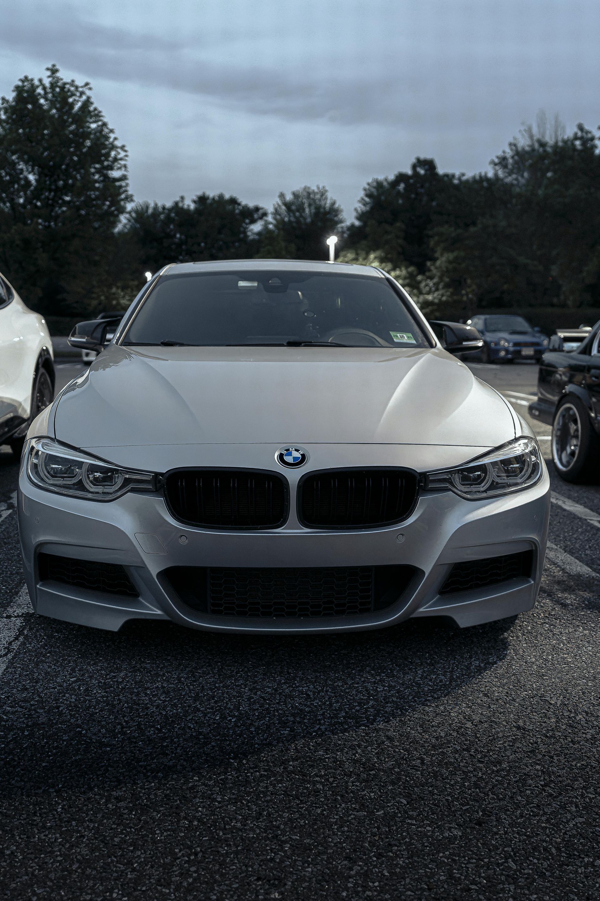 Silver BMW sedan parked in a lot, front view, black grill, overcast sky.