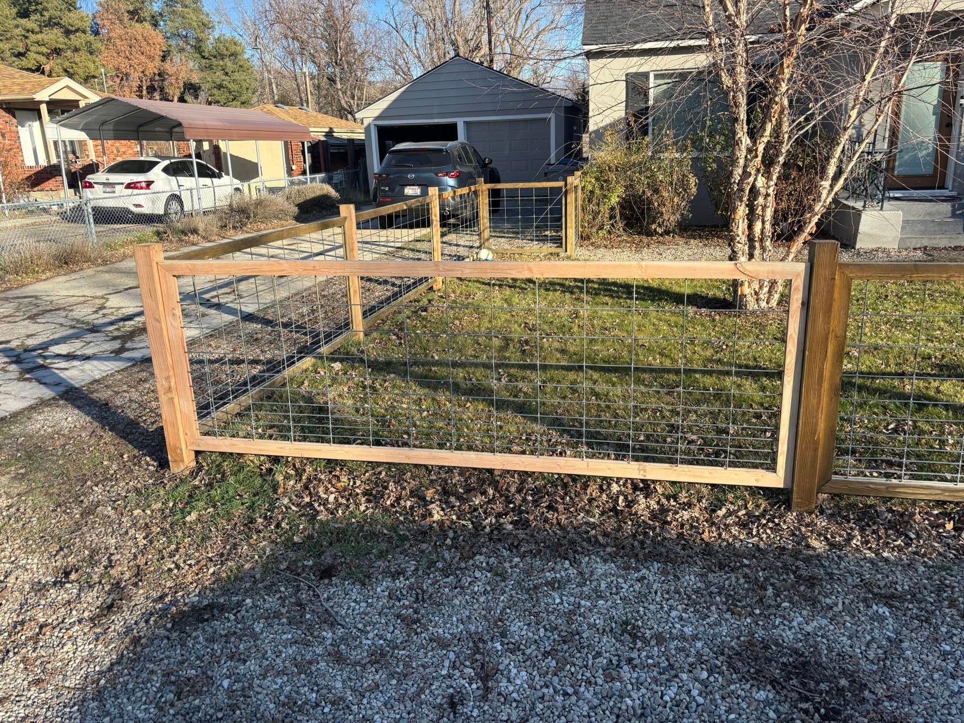Wooden fence enclosing a small lawn; a car is parked in a nearby driveway, and a garage is visible in the background.