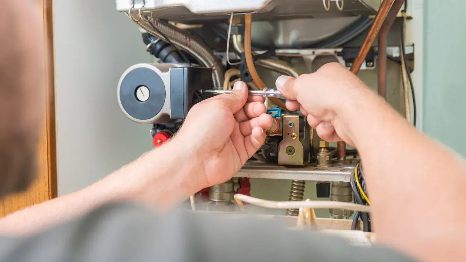 A man is fixing a boiler with a screwdriver.