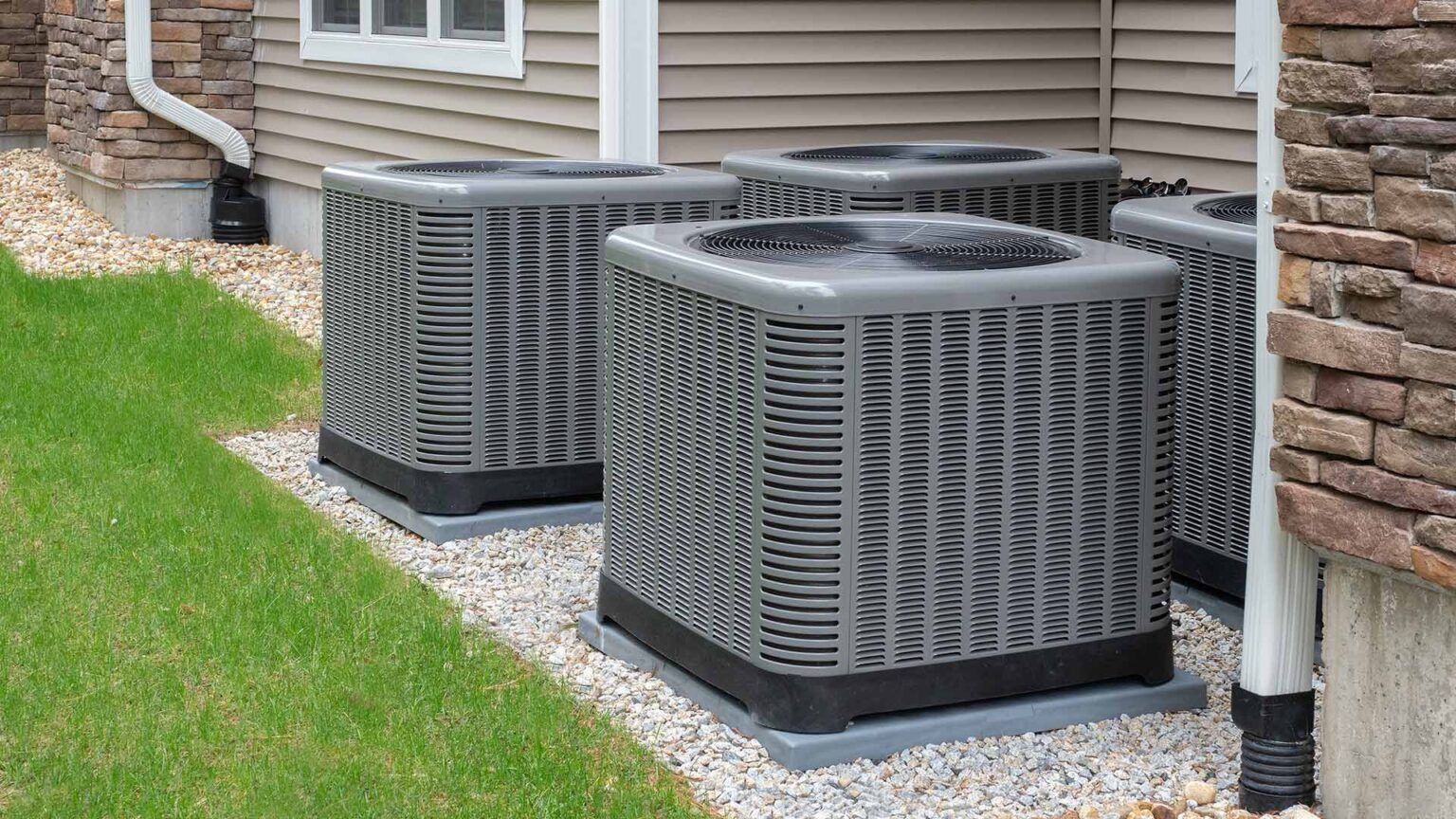 Three air conditioners are sitting outside of a house.