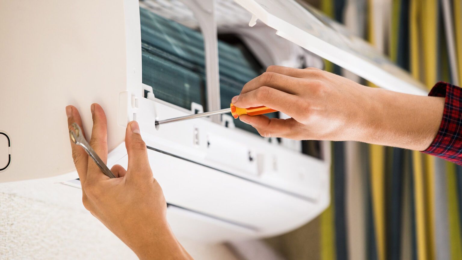 A person is fixing an air conditioner with a screwdriver.