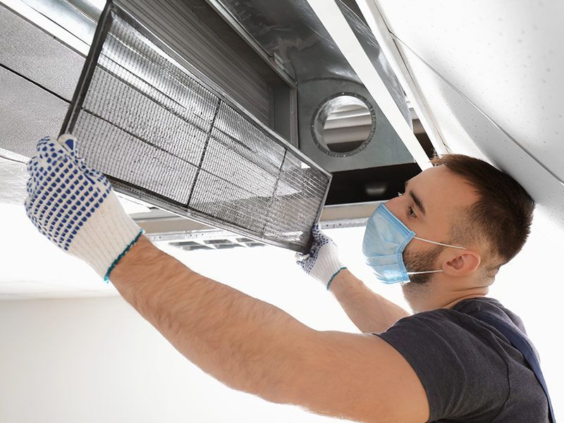 A man wearing a mask and gloves is cleaning an air duct.