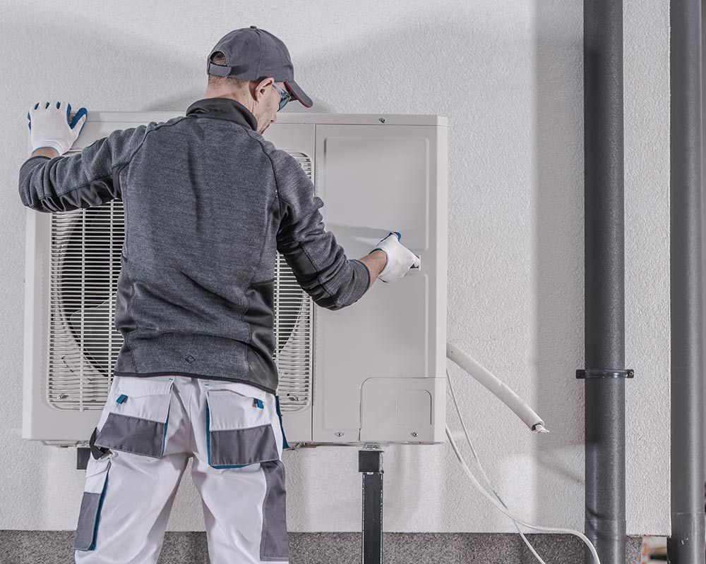 A man is installing an air conditioner on the side of a building.