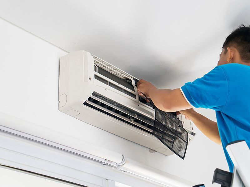 A man is working on an air conditioner on a ladder.