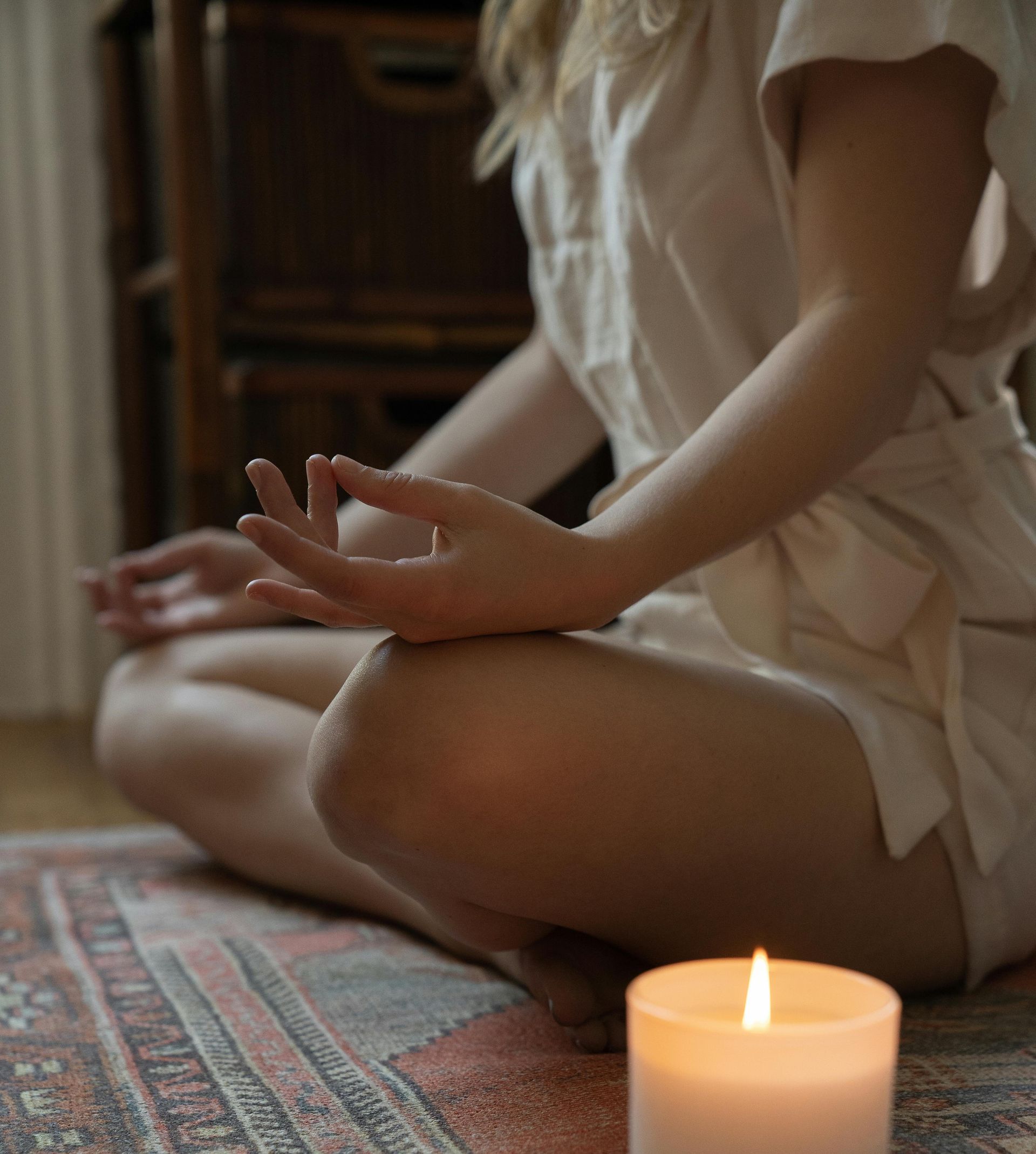 A woman is sitting on the floor with her legs crossed next to a candle.