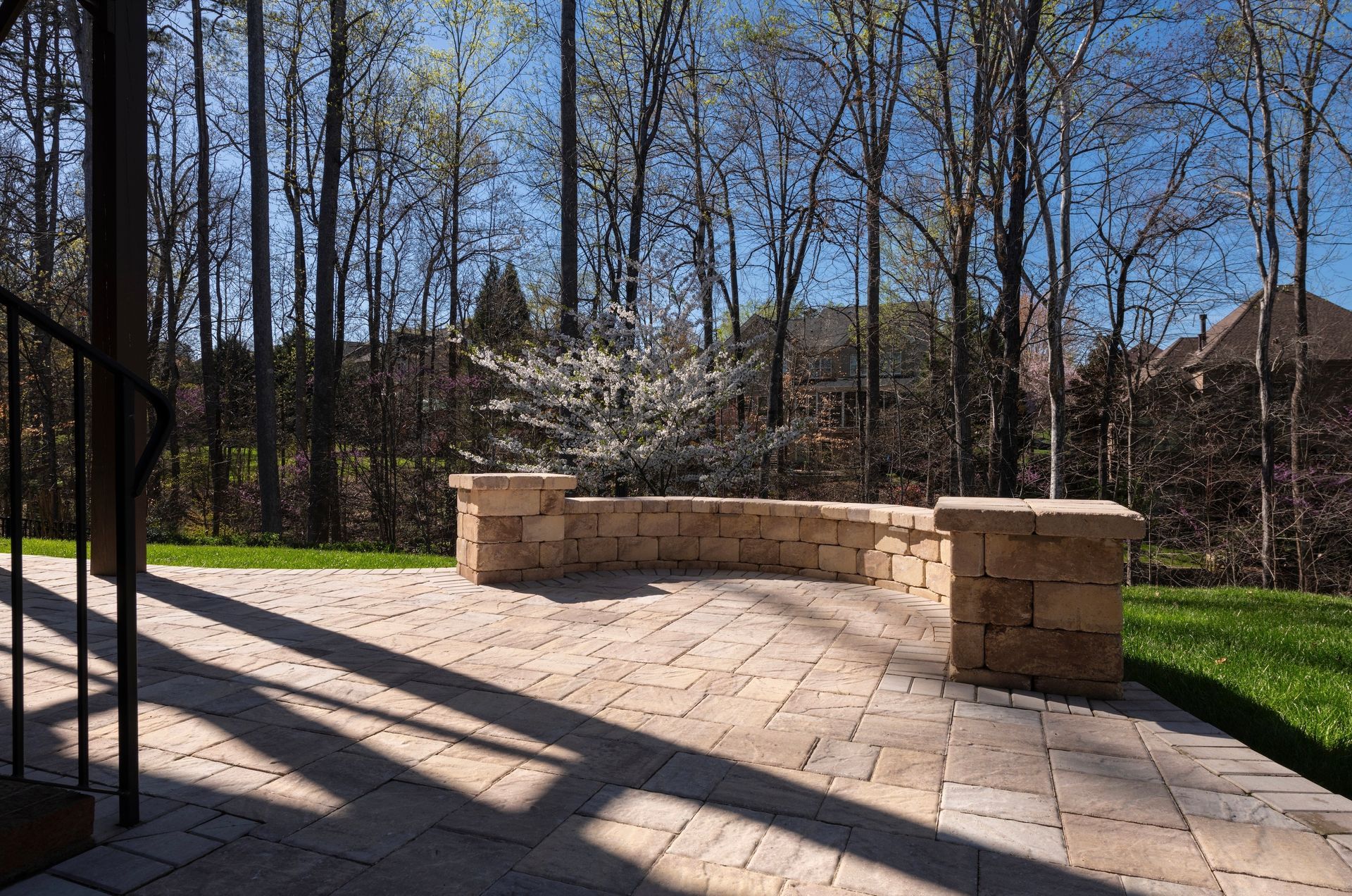 Stone patio with low brick wall, flanked by pillars. Trees in background, sunny day.