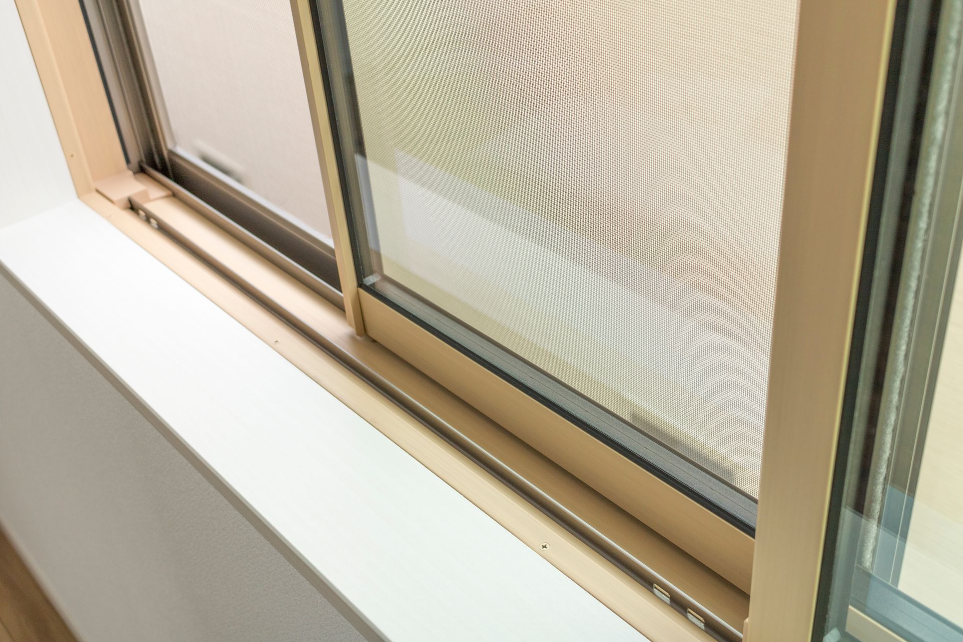 Beige sliding window with a screen partially open, set in a white windowsill.
