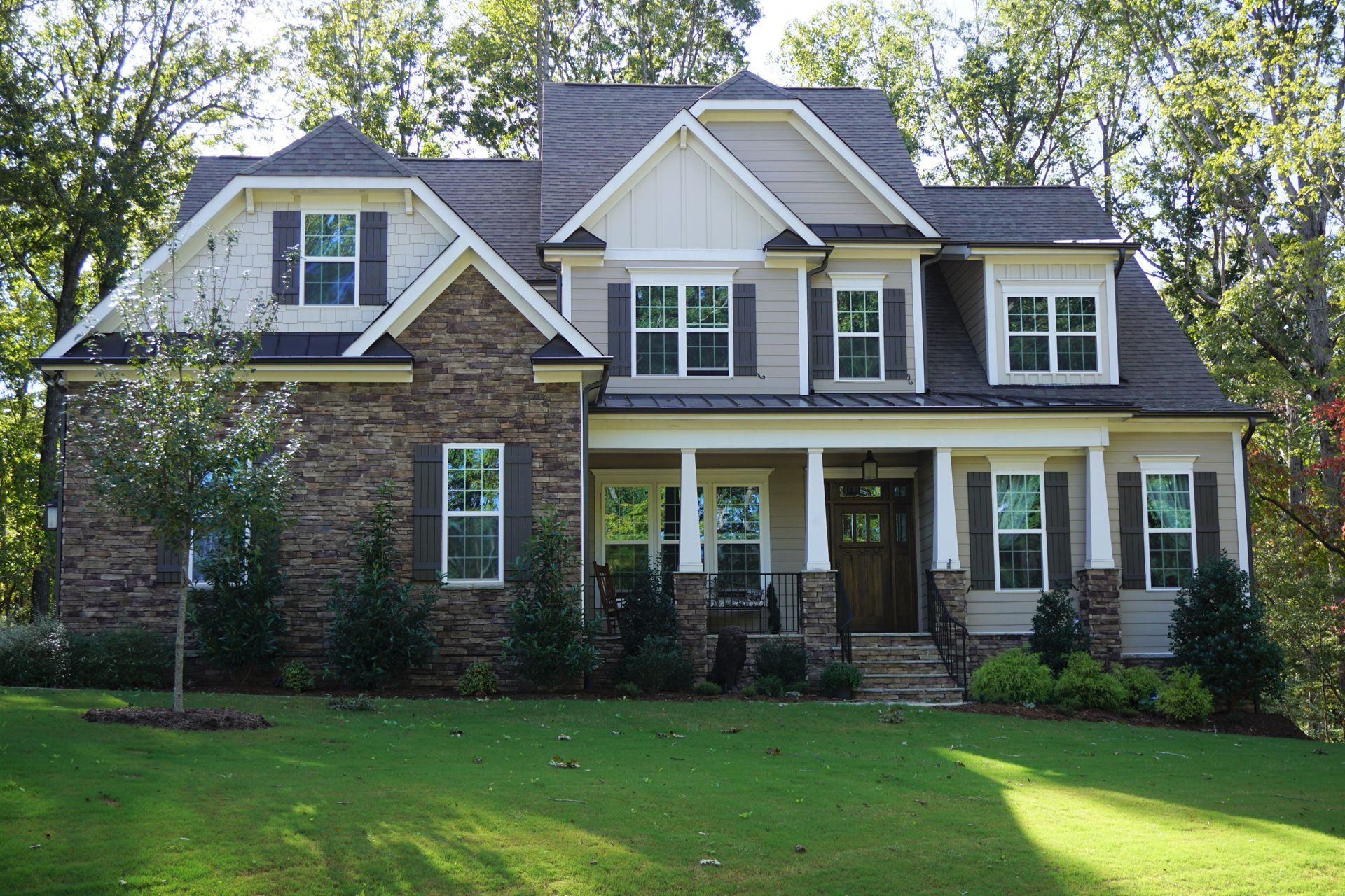 Two-story house with stone and tan siding, brown shutters, and a green lawn.
