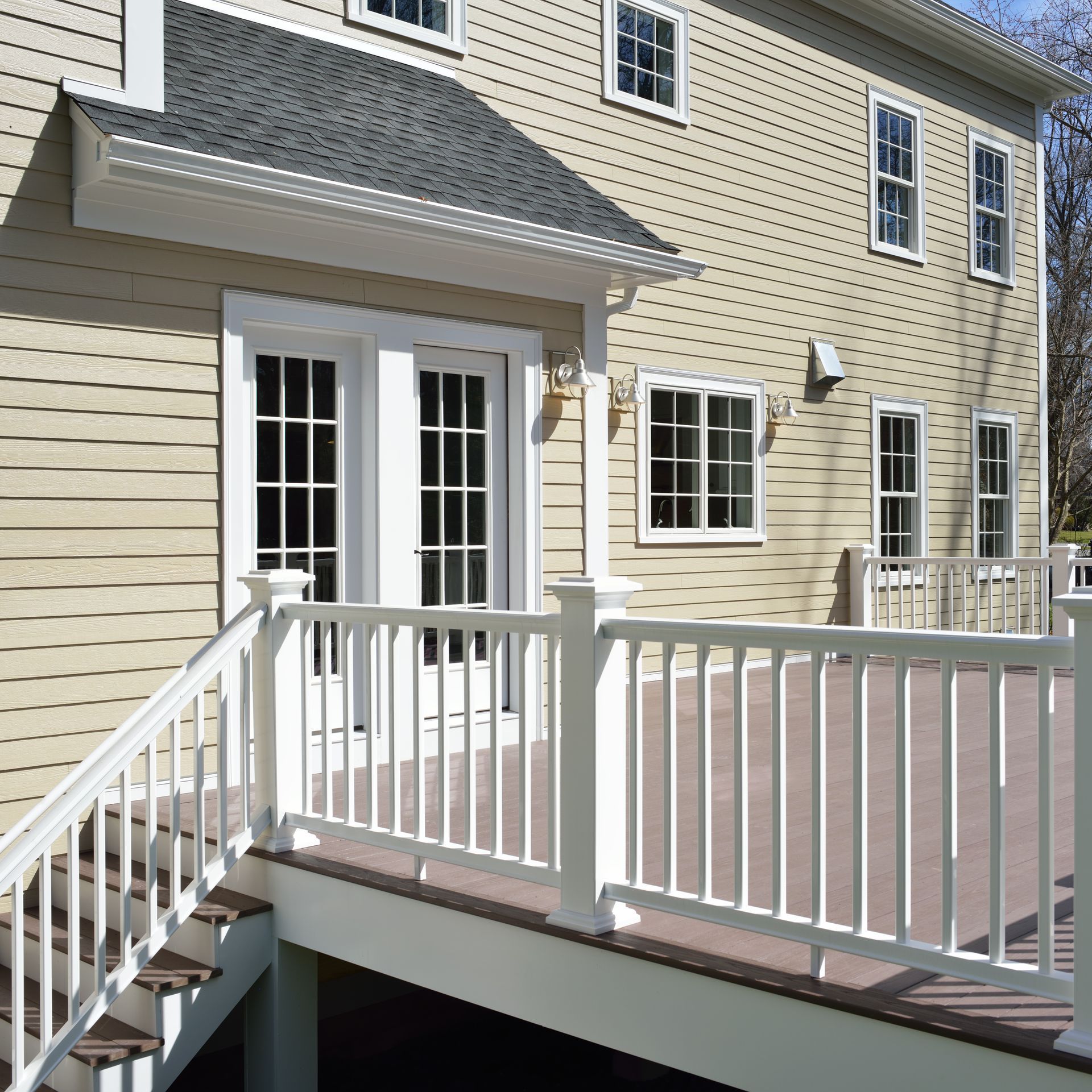 Exterior view of a beige house with white trim, a deck, and stairs.