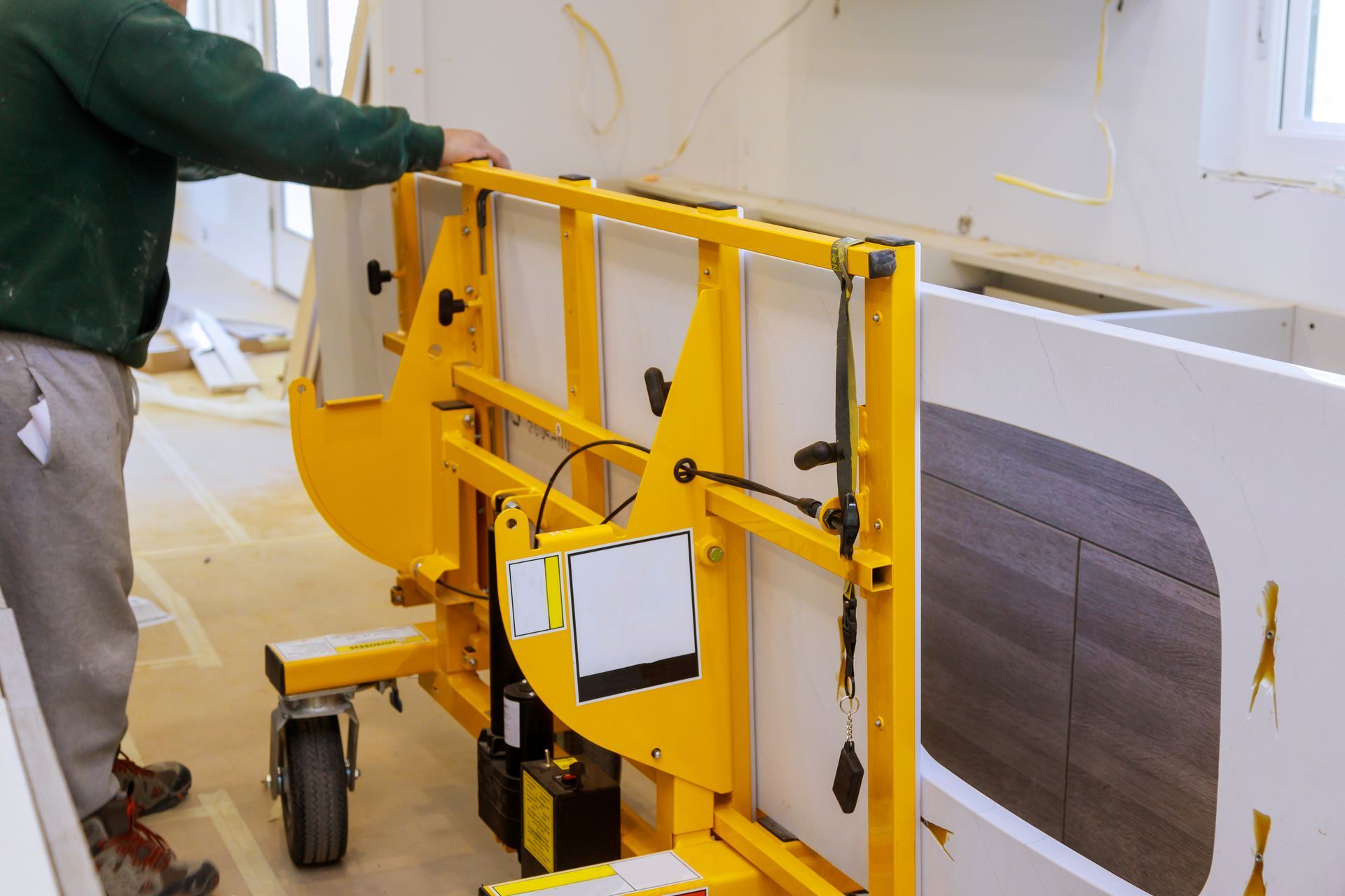 Person using a yellow cutting tool to work on a white surface in a construction setting.