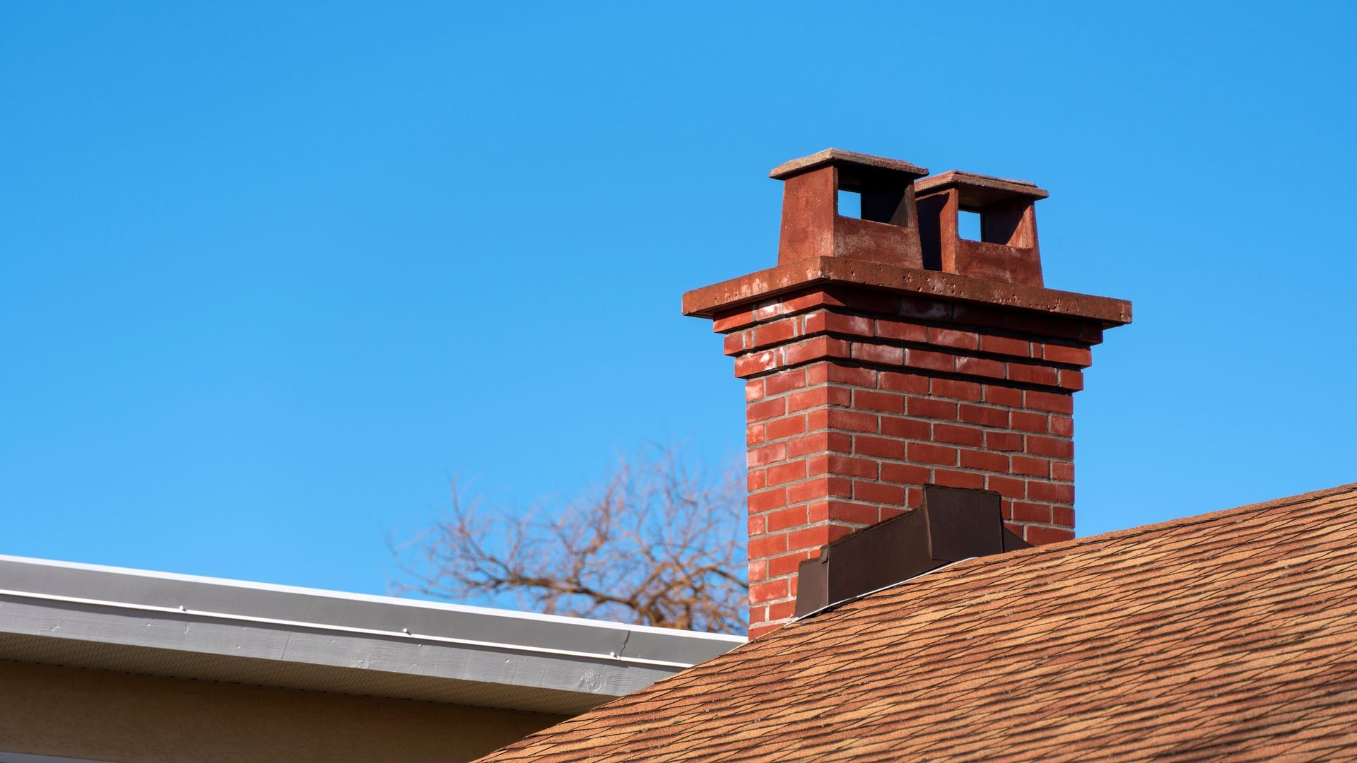 Red brick chimney on a brown roof against a clear blue sky.