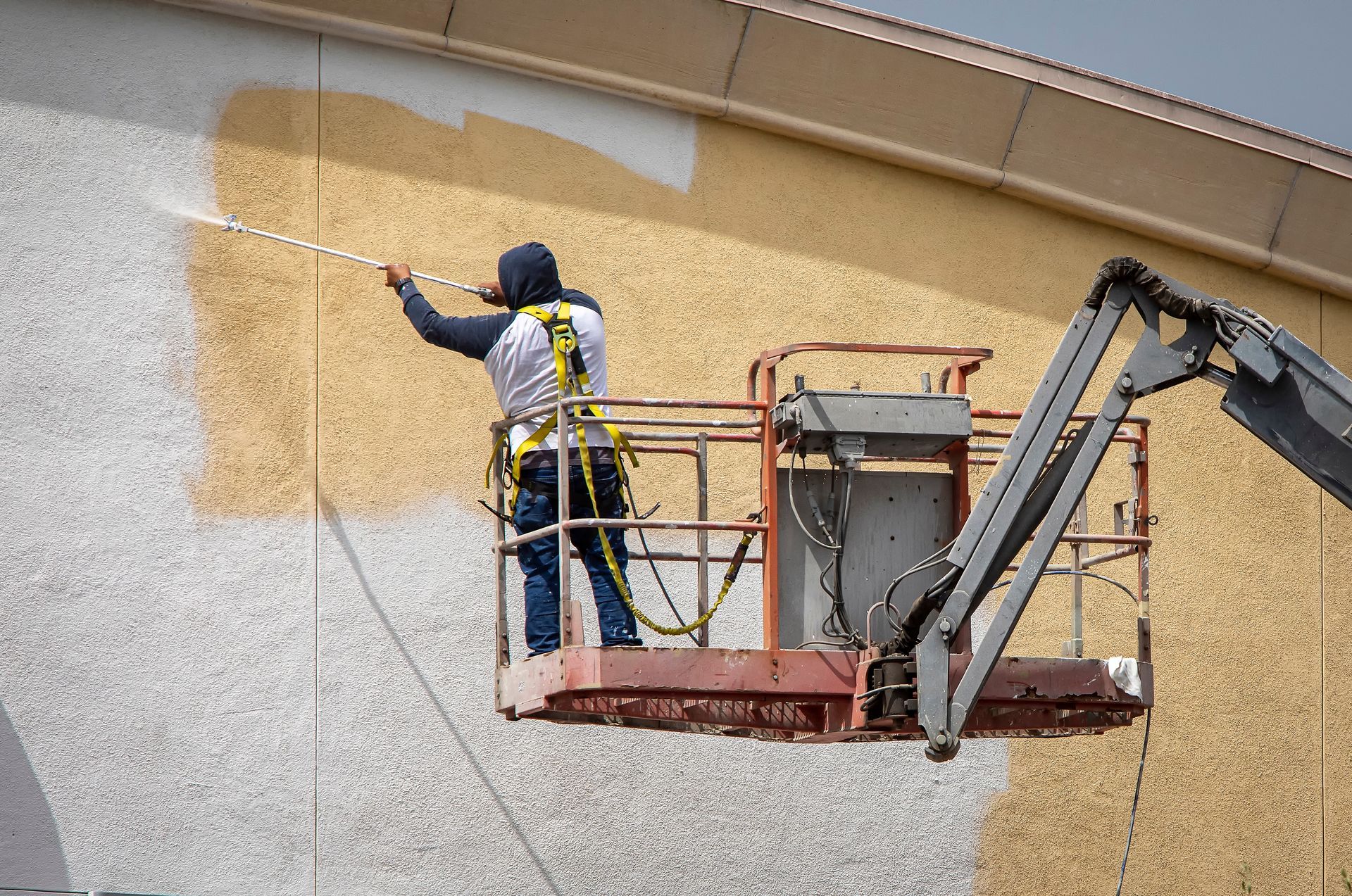 Person spraying paint on a building exterior from an aerial lift.