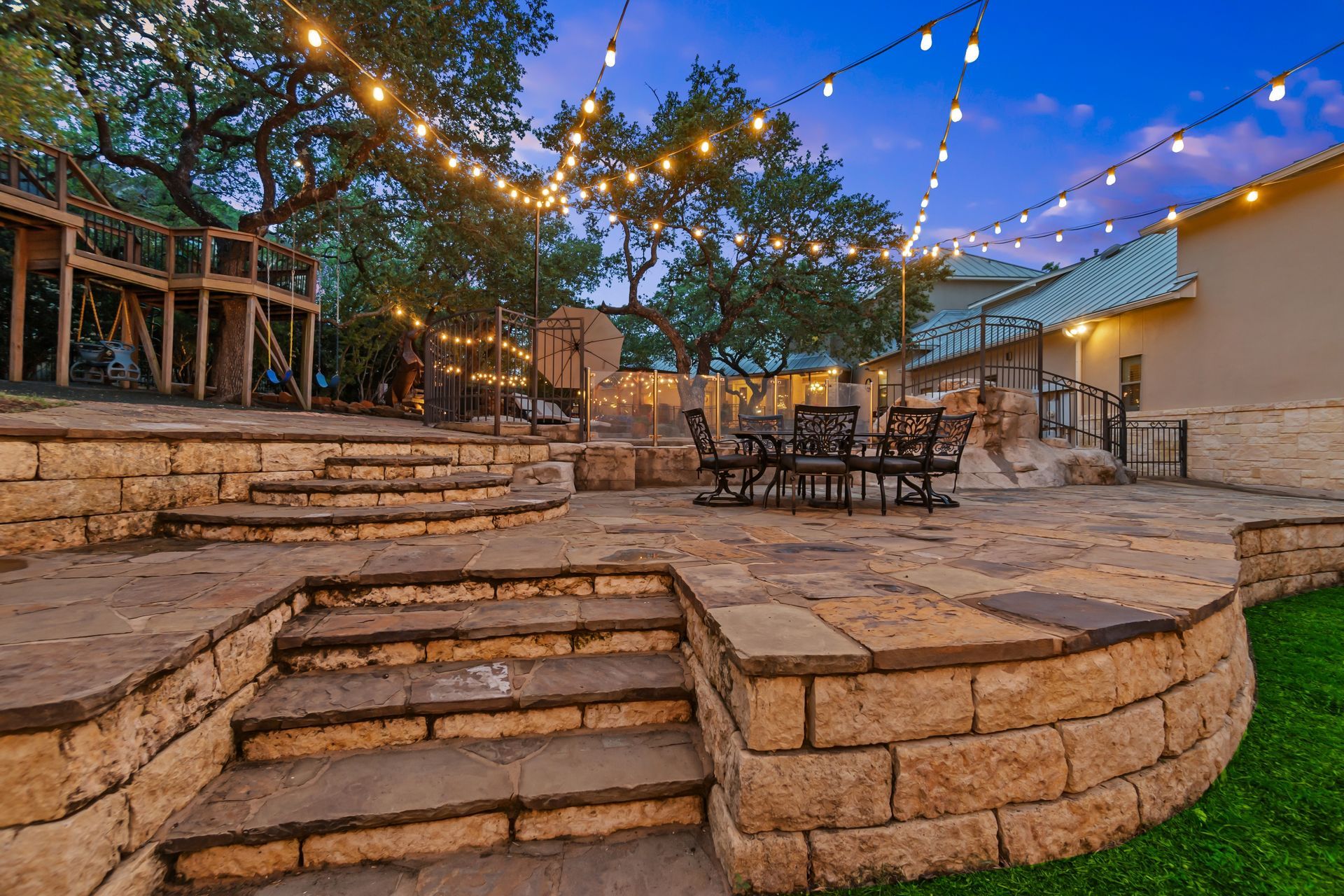 Stone patio with steps, outdoor seating, and string lights at dusk.