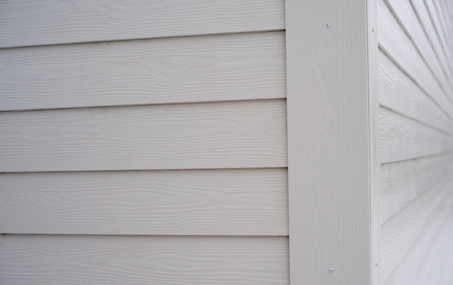 Close-up of white siding on a building's exterior corner, showing horizontal planks and vertical trim.