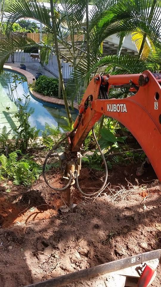 A Small Orange Excavator Is Digging A Hole In The Ground Next To A Pool — Absolute Dingo Services in White Rock, QLD