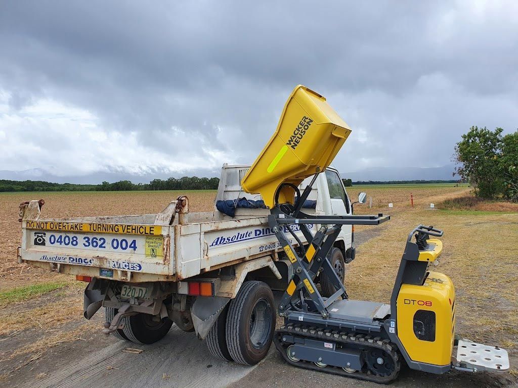 A Yellow Minu Dumper Is Parked Beside A Dump Truck — Absolute Dingo Services in White Rock, QLD