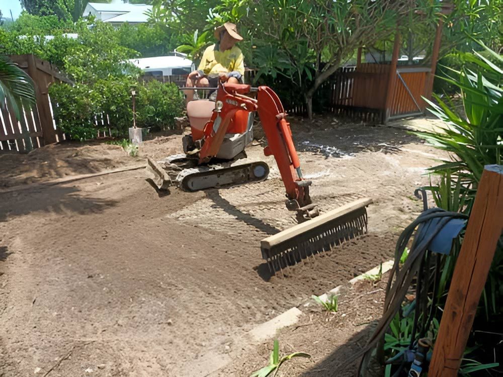 A Man Is Driving A Small Excavator In A Backyard — Absolute Dingo Services in White Rock, QLD