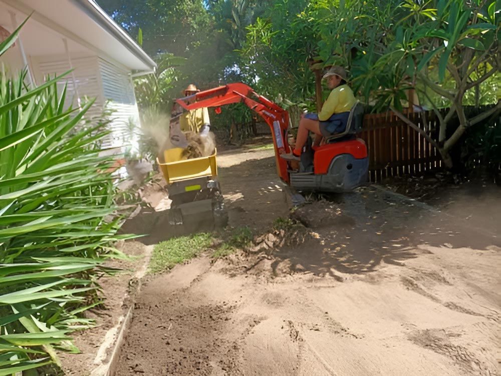 A Man Is Driving A Small Excavator Down A Dirt Road — Absolute Dingo Services in White Rock, QLD