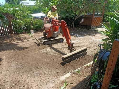 A Man Is Driving A Small Excavator In A Backyard — Absolute Dingo Services in White Rock, QLD