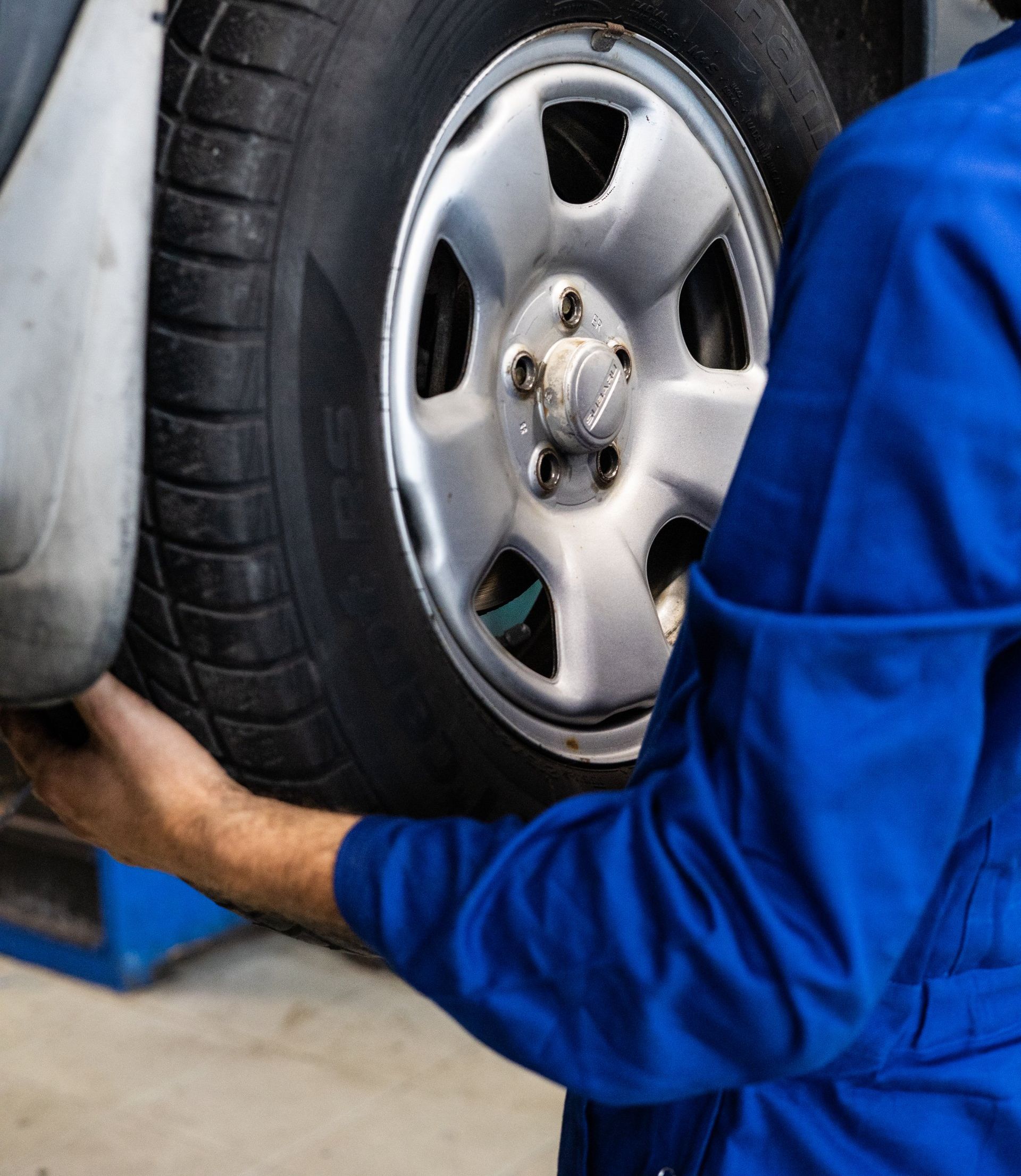 A man in a blue uniform is working on a car tire
