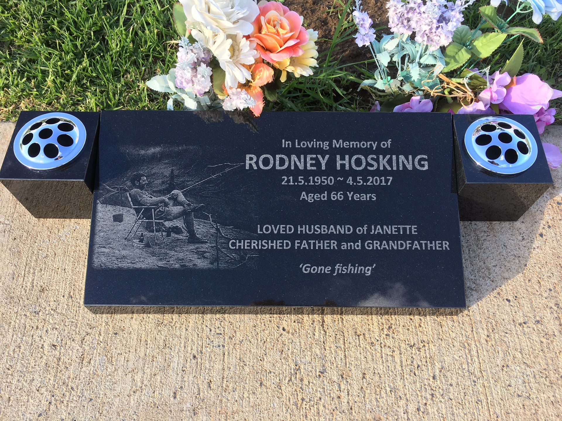 A gravestone for rodney hoskin is surrounded by flowers