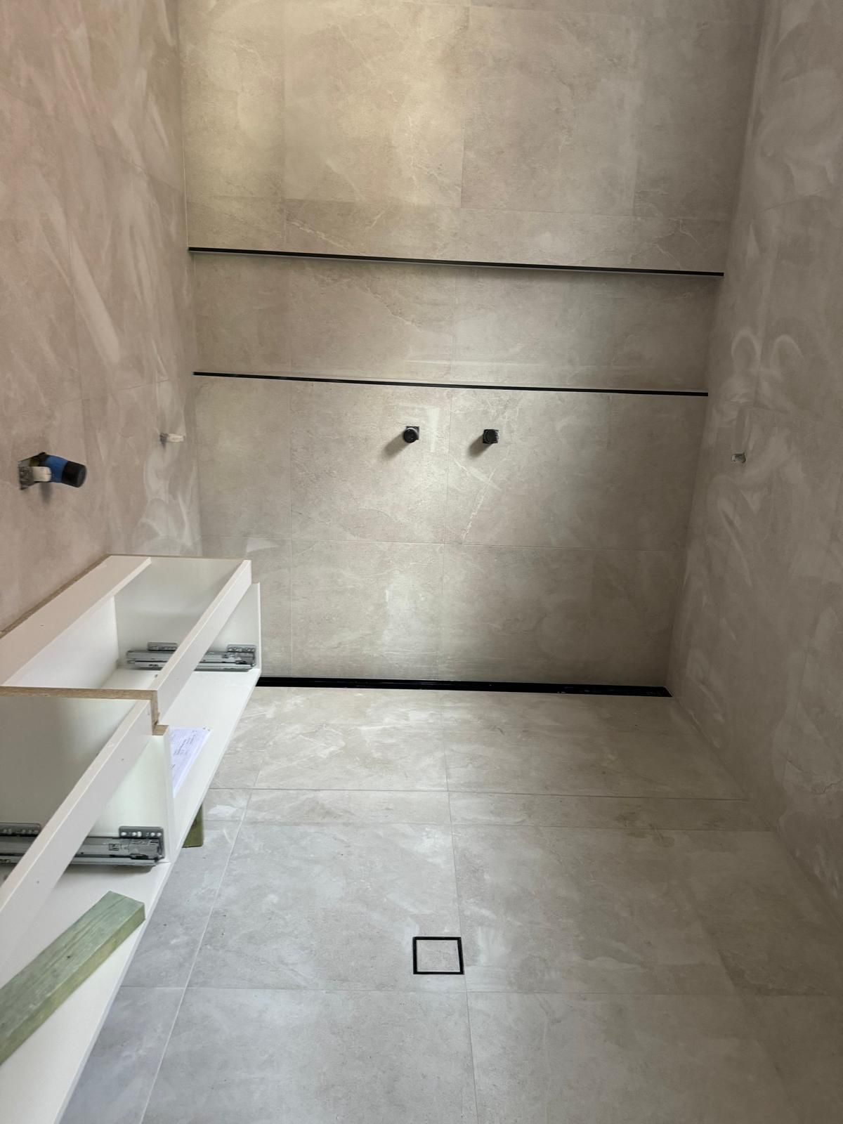 Modern shower interior with light gray tile and black trim, featuring a built-in shelf.