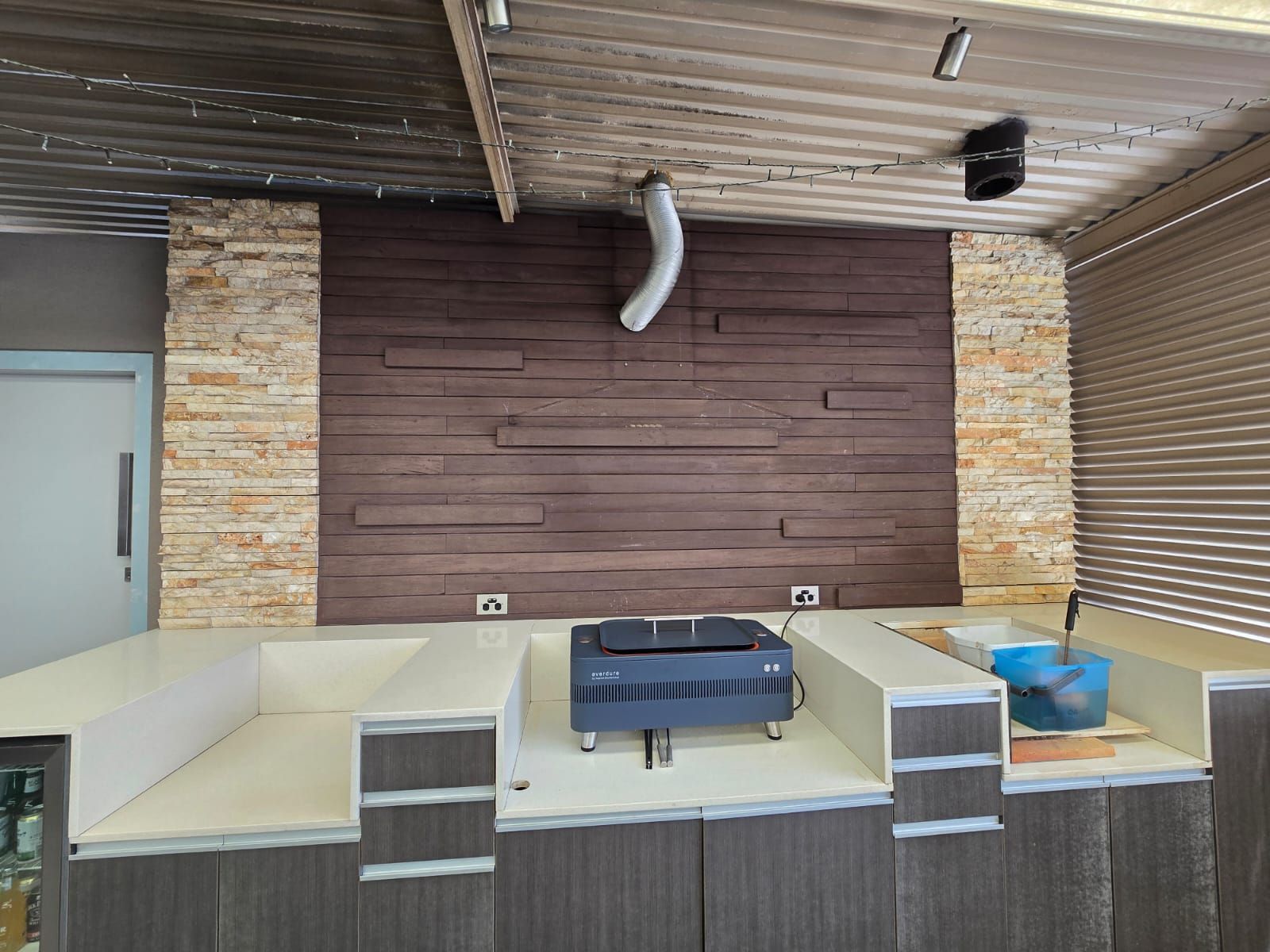 Indoor kitchen with a dark brown wood-paneled wall, tan countertop, and a black appliance.