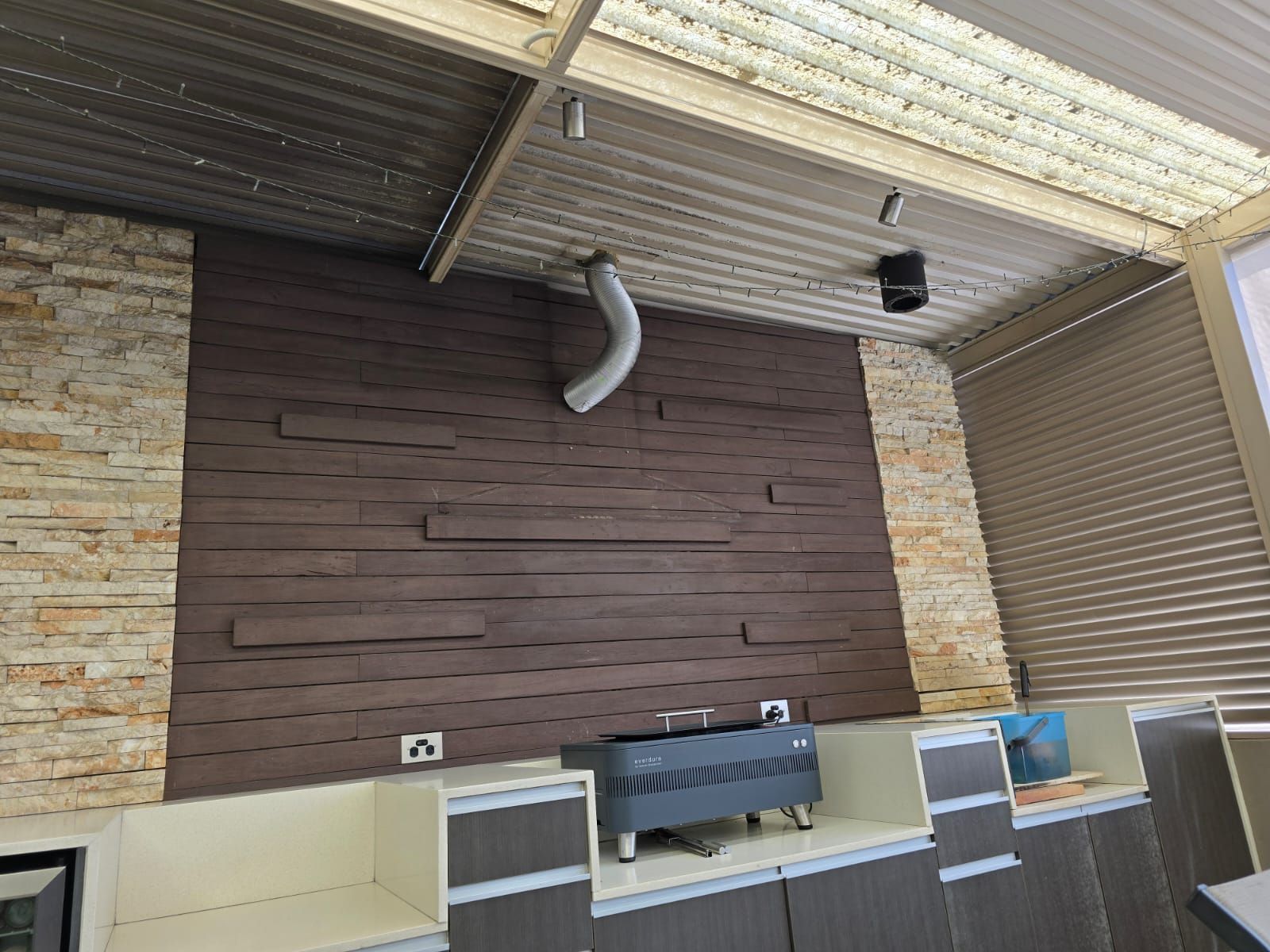 Outdoor kitchen with dark brown wall paneling, beige brick sides, and gray cabinets.
