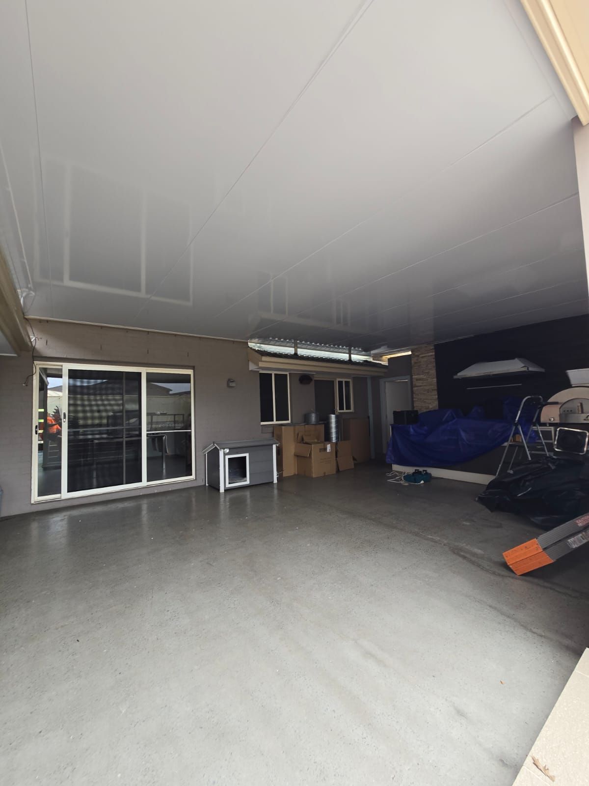 Open patio with concrete floor, sliding glass doors, and items stored near a wall.